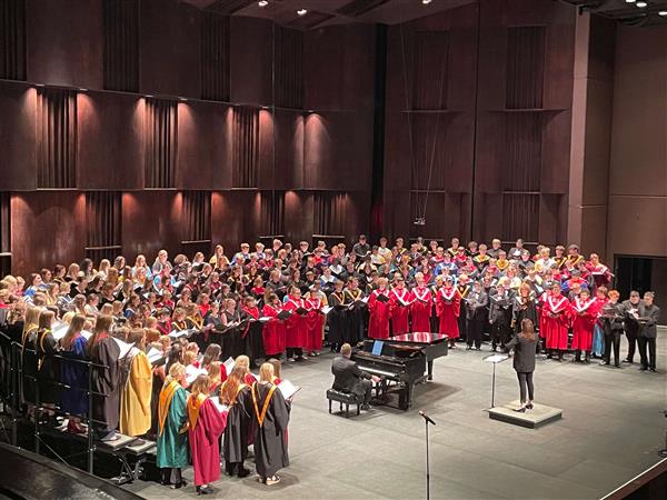Choir students stand on raisers facing a conductor and piano at Juanita K. Hammons Hall.